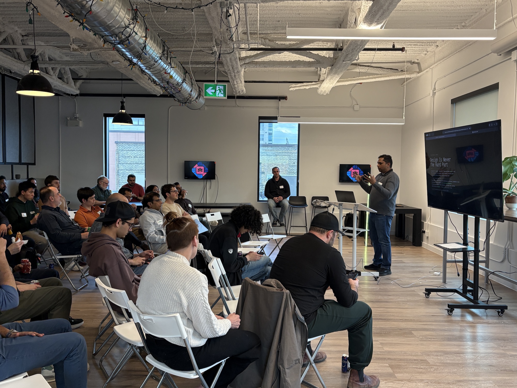 Presenter holding up a device next to a screen of terminal output while the audience takes notes